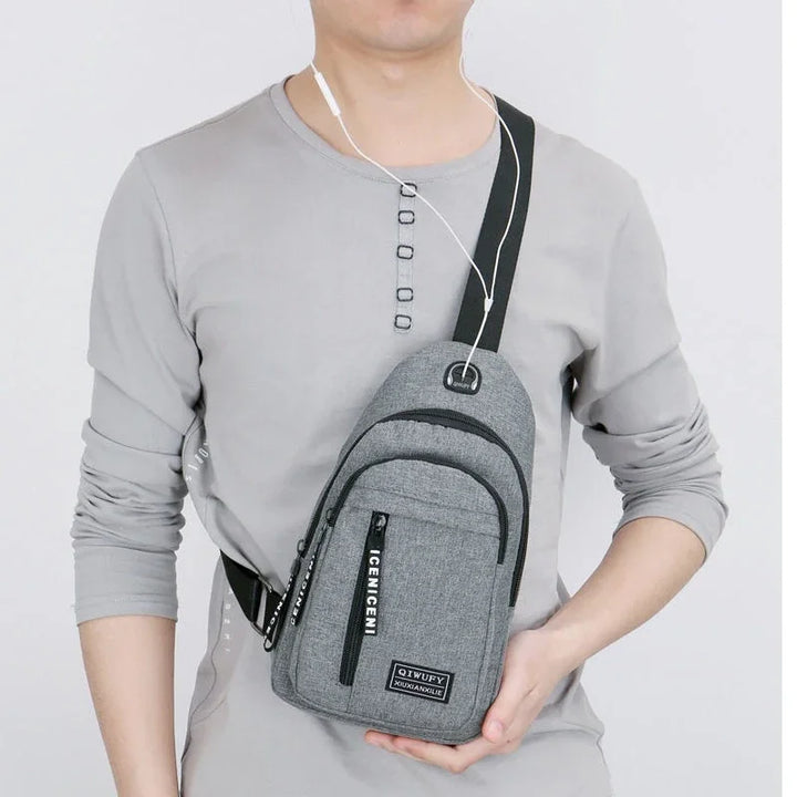 Man wearing a gray crossbody sling bag with black zippers and white text on the front pocket