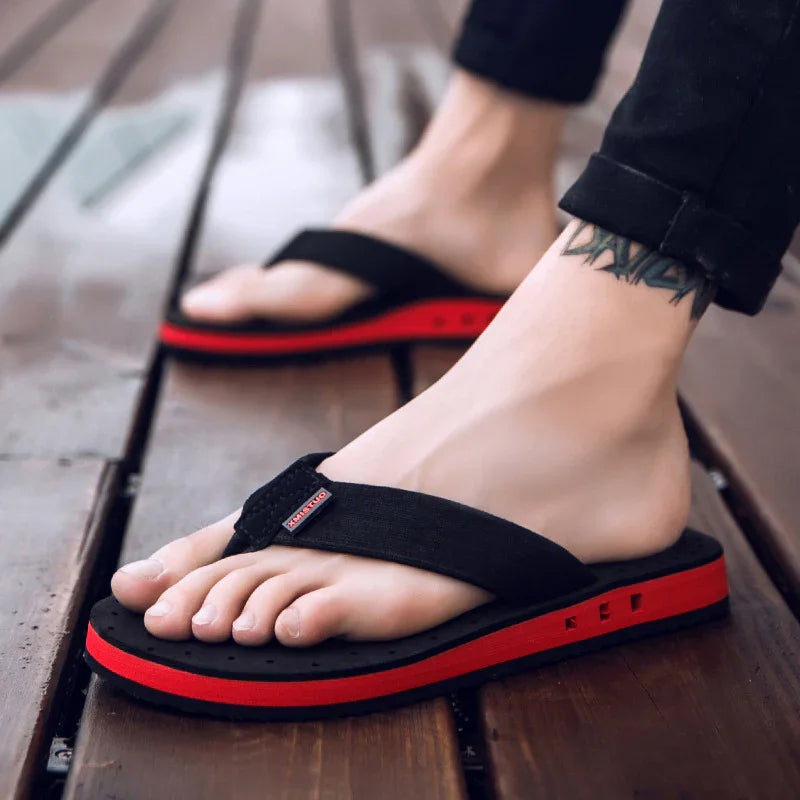 Close-up of feet wearing black and red flip-flops with wood floor background, tattoo visible