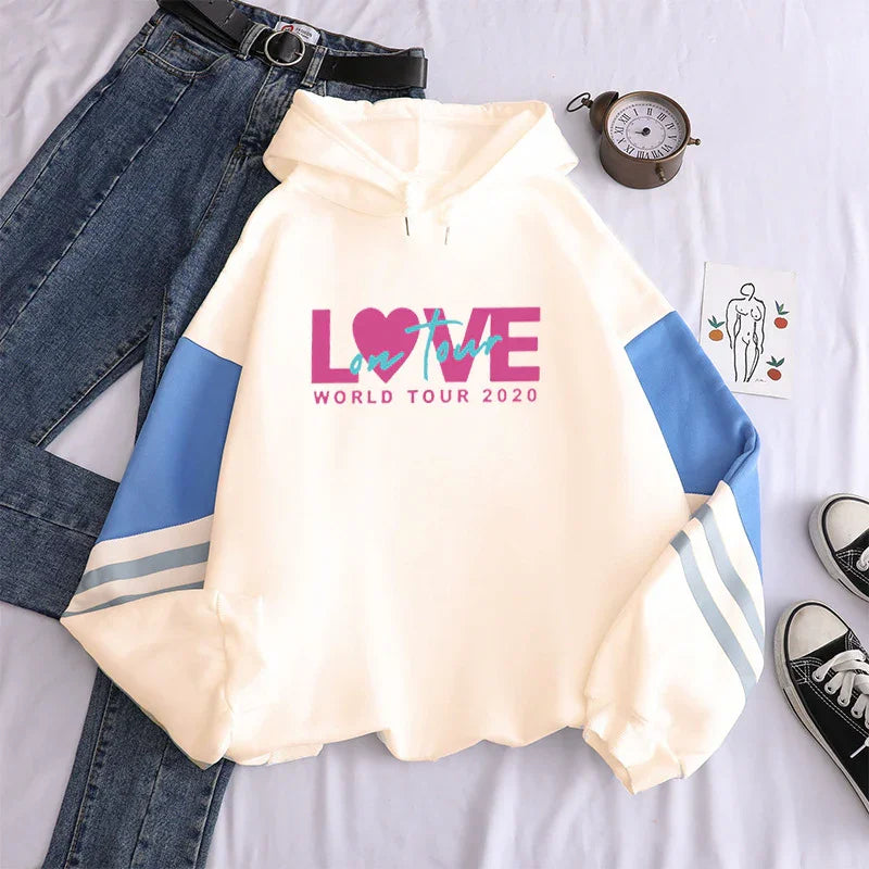 Cream hoodie with blue sleeves and 'Love on Tour World Tour 2020' text, styled with jeans and sneakers