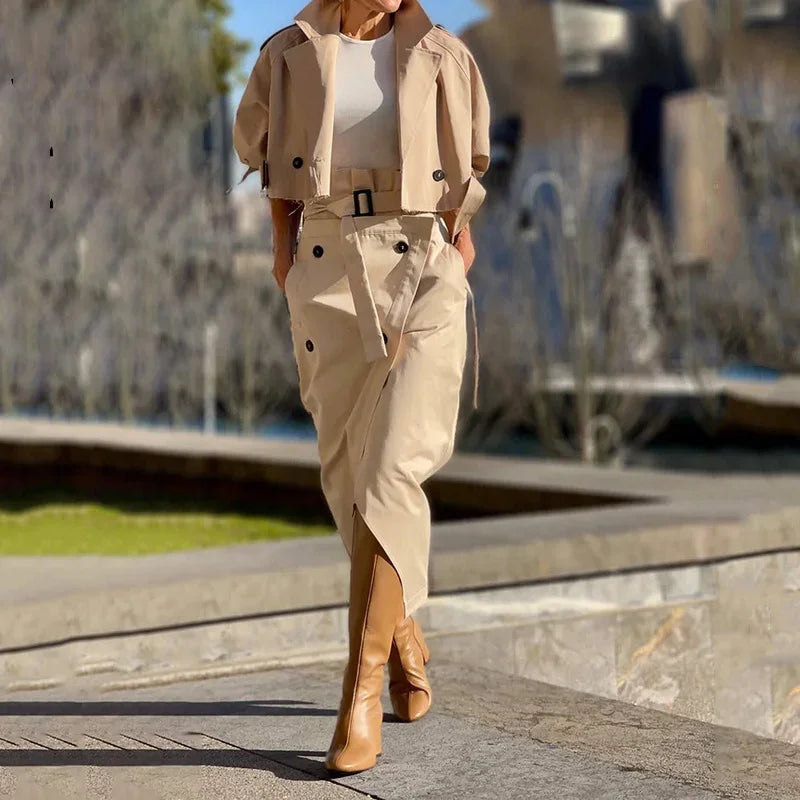 Woman walking outdoors wearing beige cropped trench coat, belted skirt, and tan knee-high boots