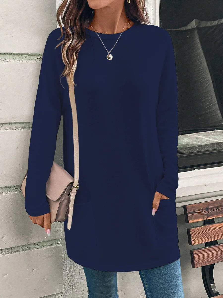 Woman wearing navy long-sleeve tunic dress with pocket, beige crossbody bag, and blue jeans outdoors