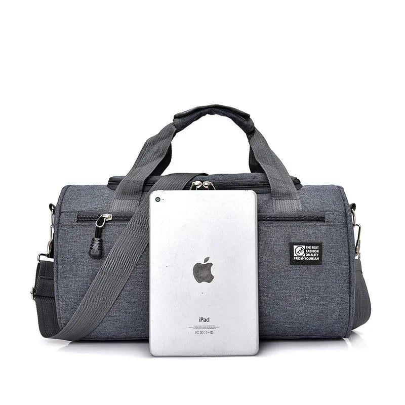 Gray travel duffel bag with handles and detachable shoulder strap, shown with silver iPad for size comparison