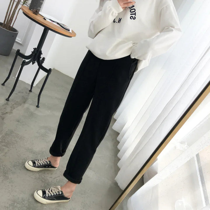 Person wearing black cropped pants and black slip-on sneakers with white soles in modern room