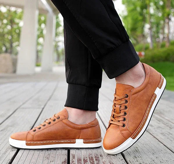 Brown leather casual sneakers with white soles worn with black jogger pants on wooden deck