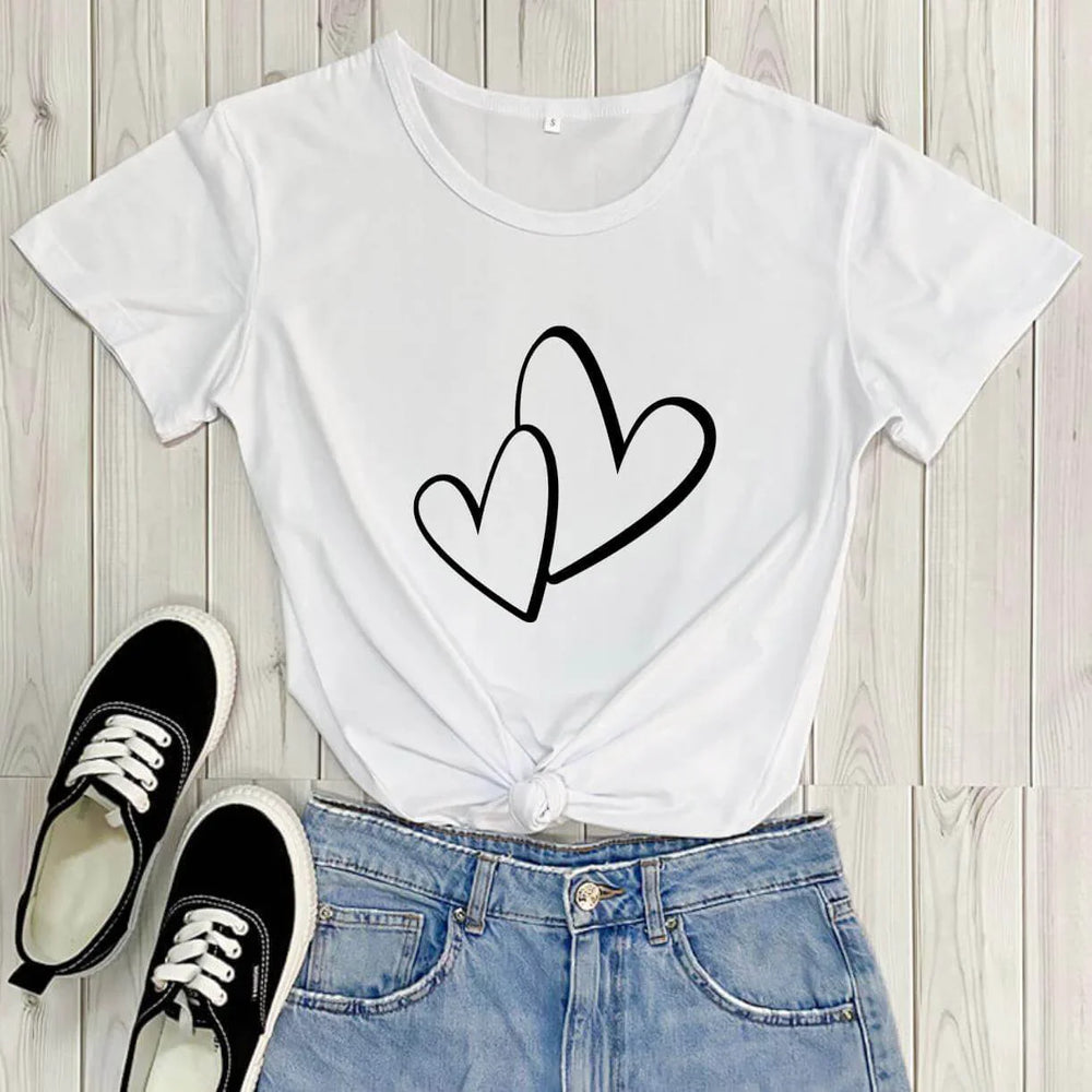 White t-shirt with two black hearts graphic paired with blue denim jeans and black canvas sneakers on wood floor