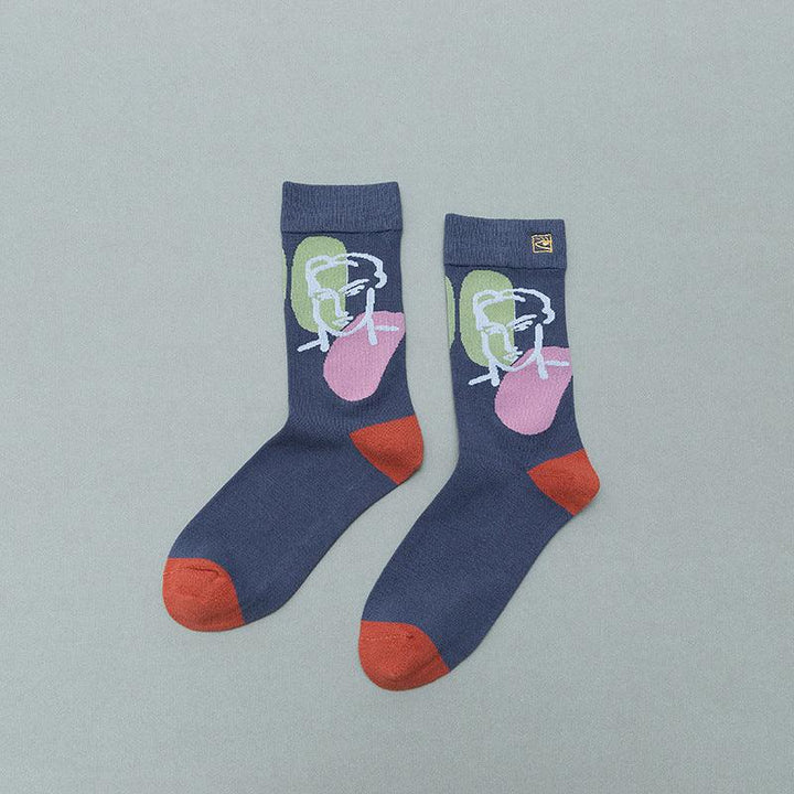 Pair of navy blue socks with red toes and heels, featuring abstract face art in white, green, and pink