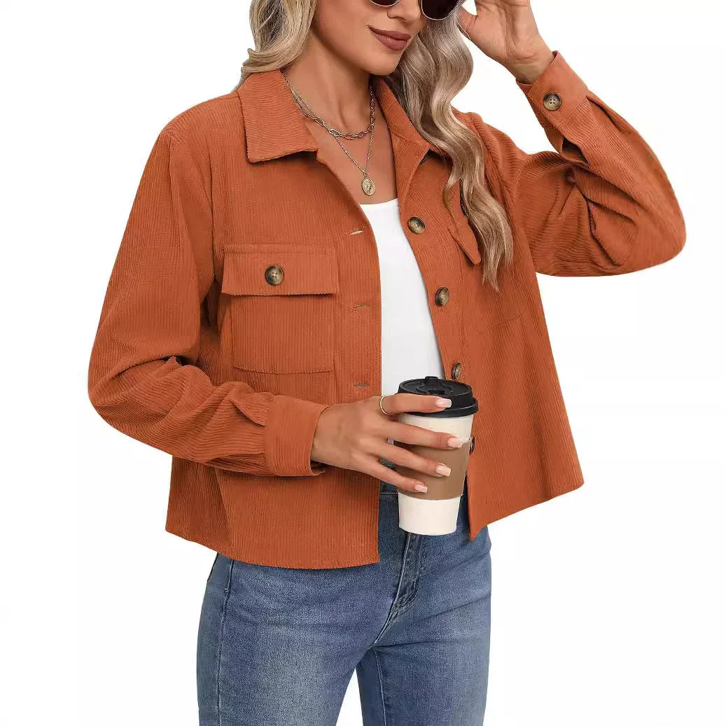 Woman wearing rust orange corduroy jacket over white top and blue jeans holding a coffee cup