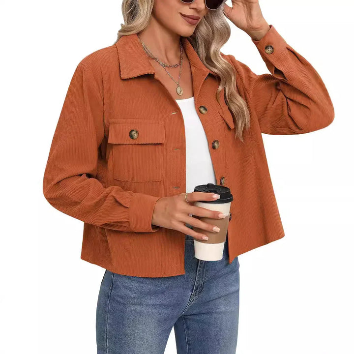 Woman wearing rust orange corduroy jacket over white top and blue jeans holding a coffee cup