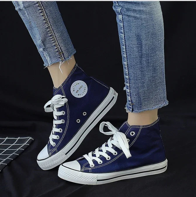 Navy blue high-top canvas sneakers with white laces worn with frayed light blue jeans on black background
