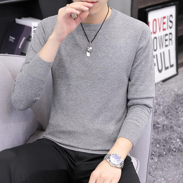 Man wearing a grey knit sweater, black pants, silver watch, and pendant necklace sitting on a gray chair