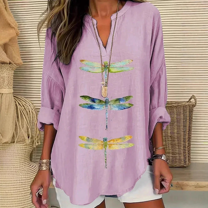 Woman wearing light purple long-sleeve shirt with colorful dragonfly prints and white shorts