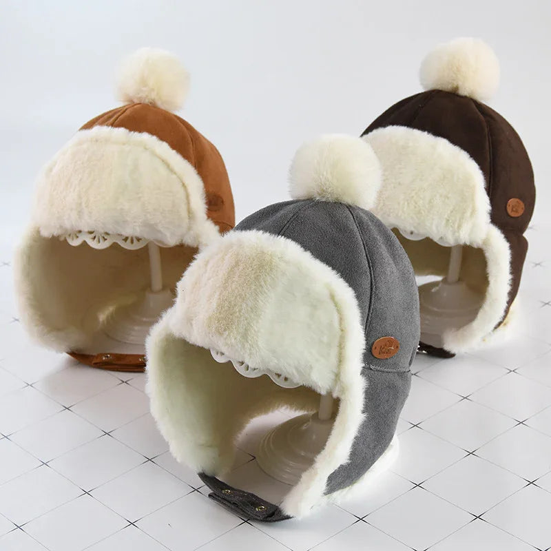 Three winter trapper hats with fluffy white fur lining and pom-poms in brown, grey, and dark brown colors