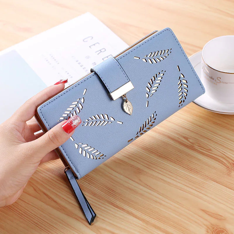 Hand holding a blue leather wallet with leaf cutout design and silver leaf charm on wooden table