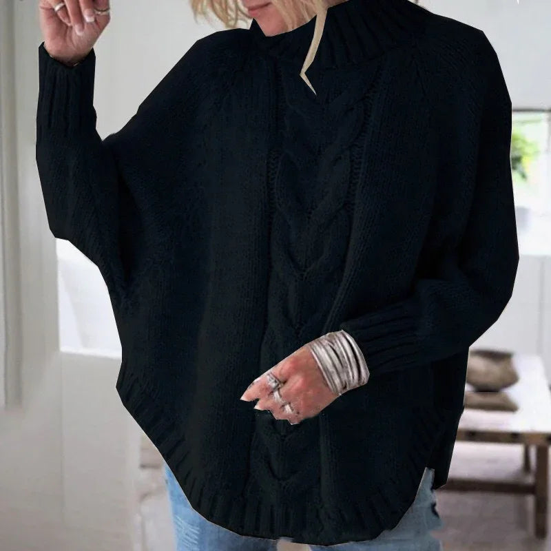 Woman wearing black cable knit poncho sweater with ribbed turtleneck and cuffs indoors