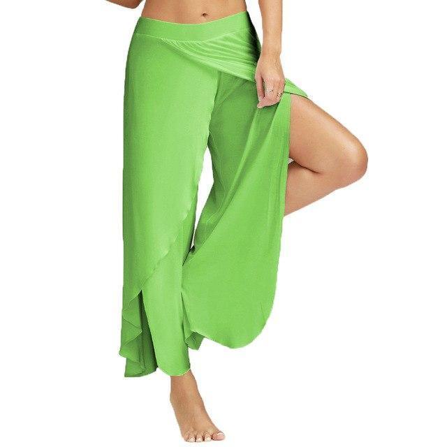 Woman wearing lime green flowy wrap pants with high slit, barefoot on white background