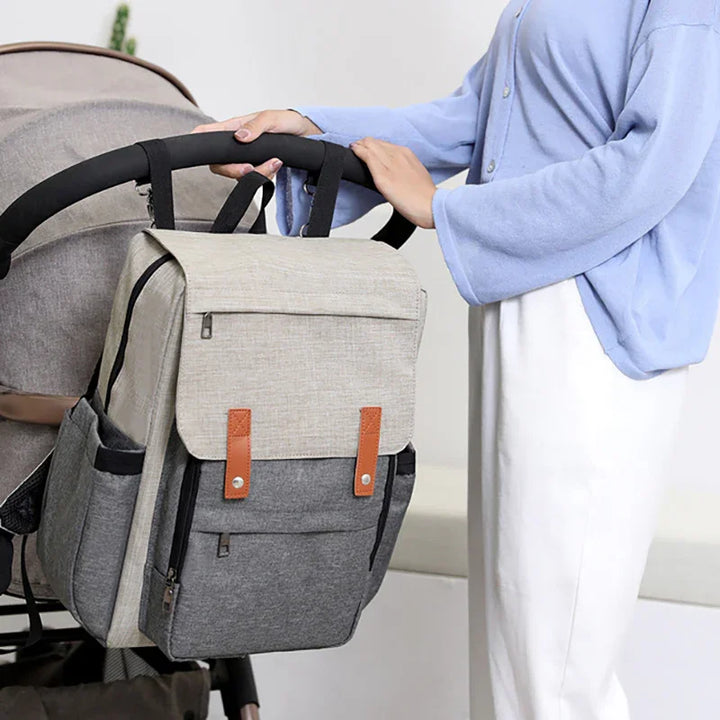 Woman in blue shirt hanging grey and beige diaper bag on black stroller handle
