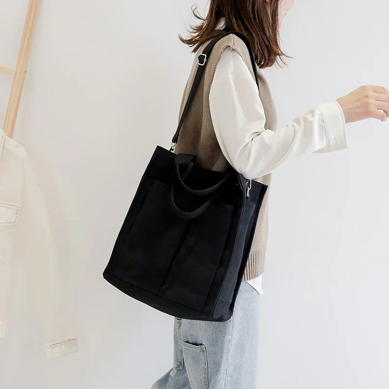 Woman wearing casual beige vest and white shirt carrying black canvas tote bag over shoulder