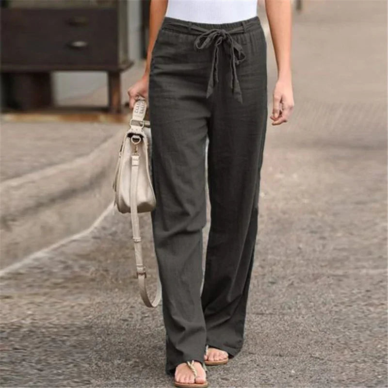 Woman wearing dark gray drawstring pants with white top and beige handbag on street