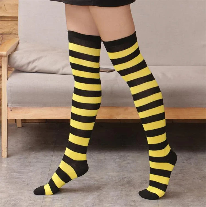 Legs wearing black and yellow striped knee-high socks on gray tile floor in front of wooden sofa