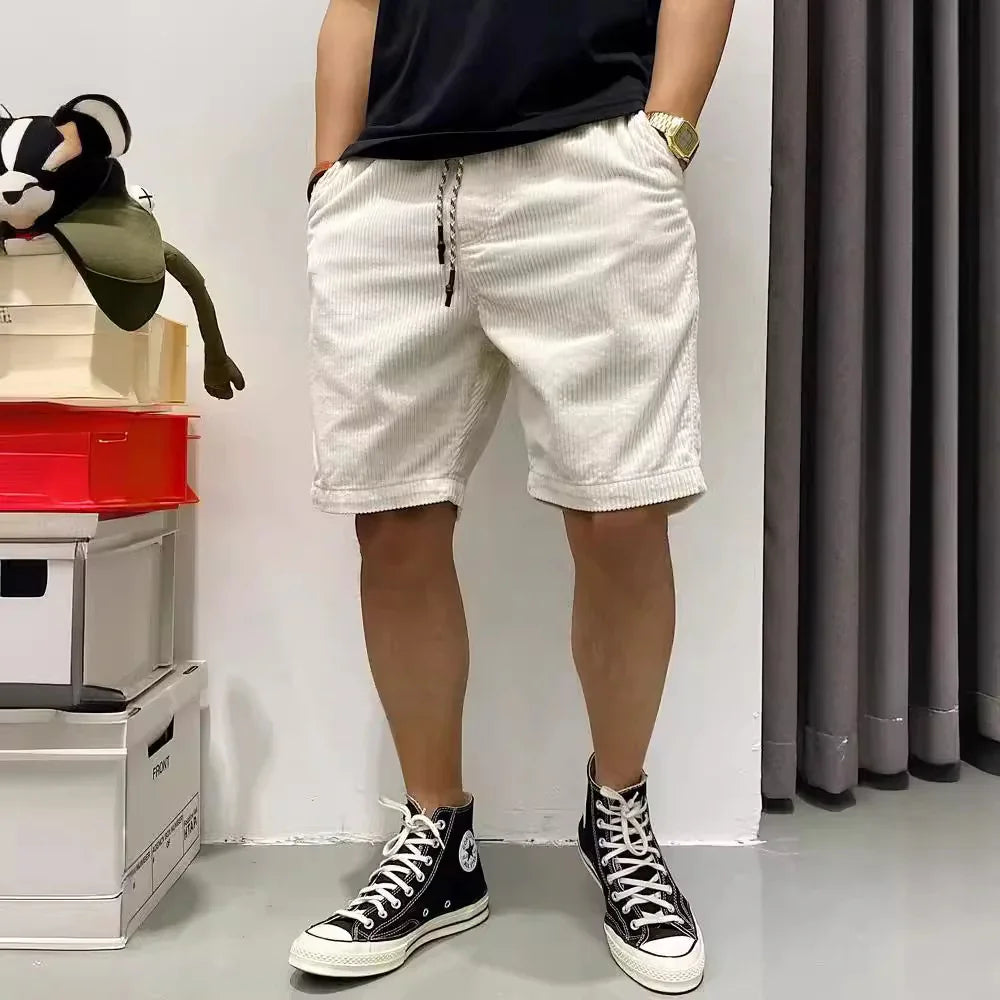 Person wearing white corduroy shorts and black high-top sneakers standing indoors next to stacked boxes
