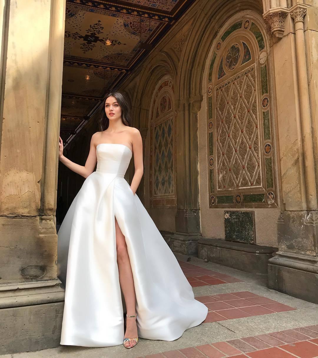 Woman in strapless white wedding gown with thigh slit standing by ornate historic arches
