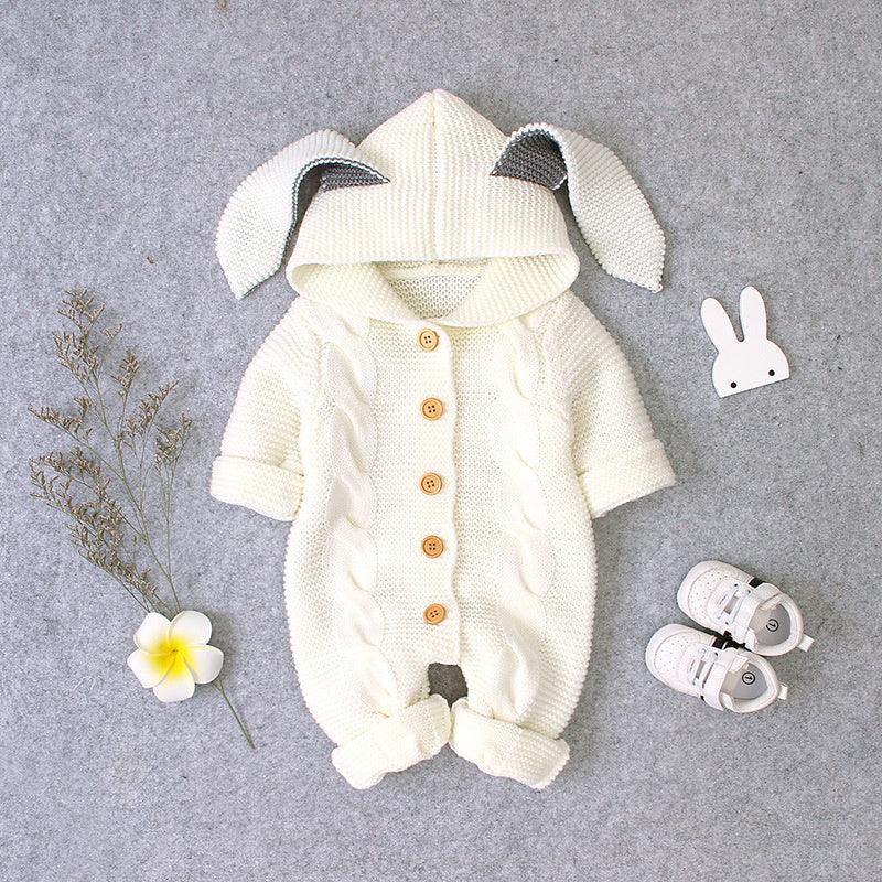 Cream knitted baby romper with bunny ears hood, wooden buttons, and white baby shoes on gray background