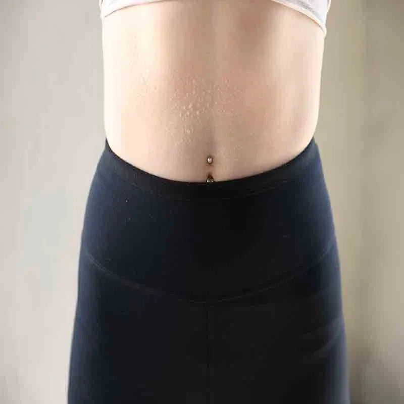 Close-up of midsection with belly button piercing, wearing black high-waisted leggings and light crop top