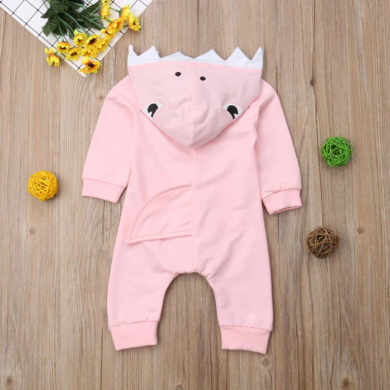 Soft pink baby onesie with dinosaur hood and tail on wood background with decorative balls