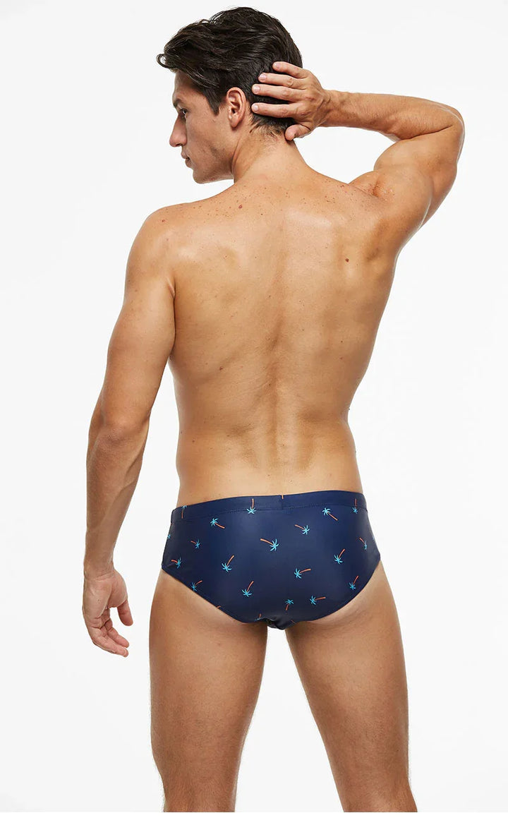 Rear view of a man wearing navy blue swim briefs with small palm tree print on white background