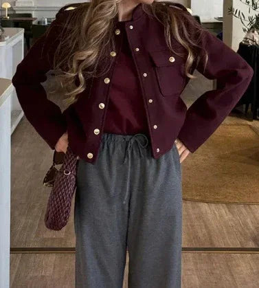 Woman wearing a burgundy button-up jacket with pockets and grey drawstring pants indoors