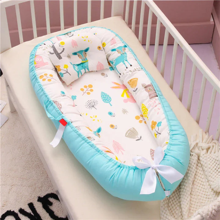 Baby nest with cute animal and floral print, turquoise padded sides, white bow, in a white crib