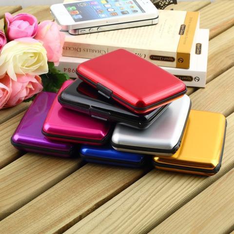 Colorful aluminum card holders stacked on wooden surface with smartphone, books, and pink flowers