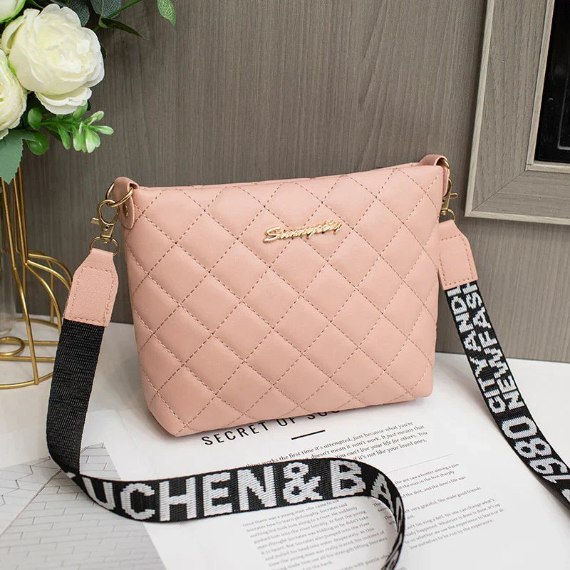 Pink quilted crossbody bag with black and white printed strap and gold brand logo