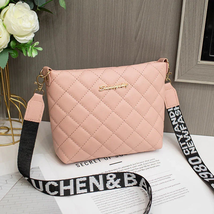 Pink quilted crossbody bag with black and white printed strap and gold brand logo