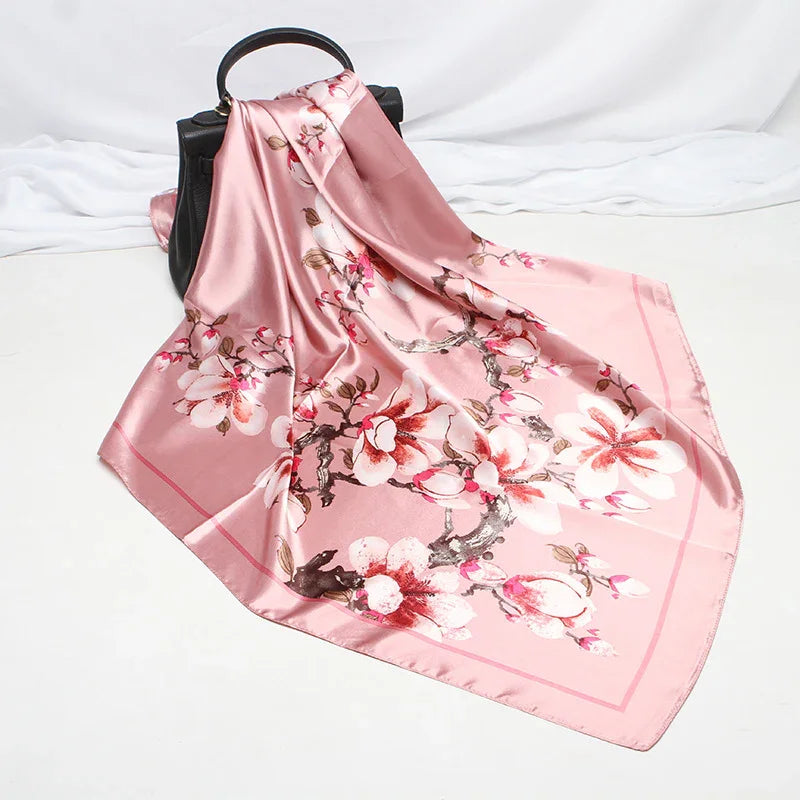 Pink silk scarf with floral cherry blossom print draped over black handbag on white surface