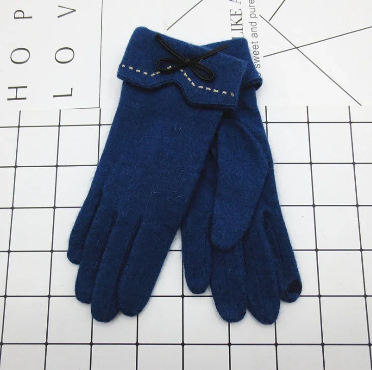 Pair of navy blue wool gloves with decorative bow and stitching detail on cuff, laid on grid background