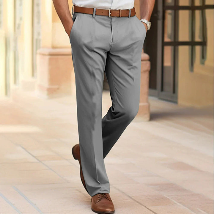 Man wearing gray dress pants with brown belt and brown leather shoes walking on stone pavement