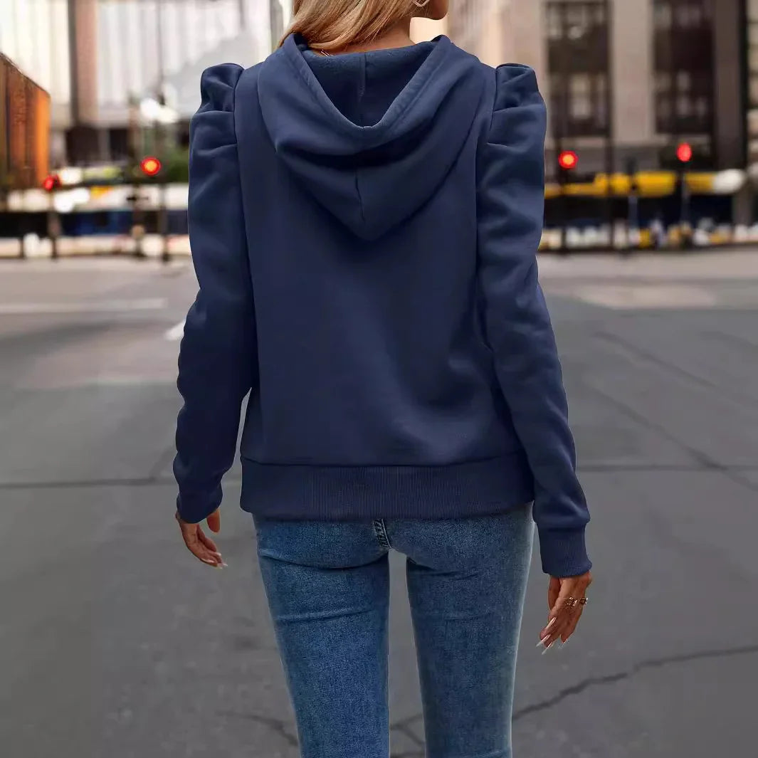 Woman wearing navy blue hoodie with puff sleeves and blue jeans walking on city street