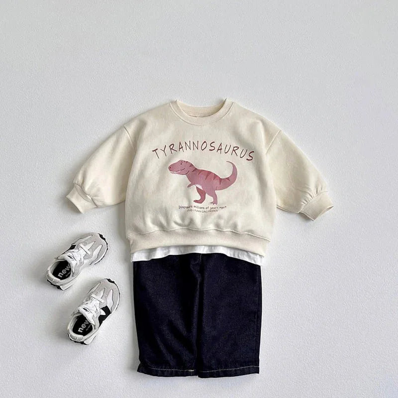 Kids outfit with cream Tyrannosaurus sweatshirt featuring dinosaur graphic, black shorts, and white sneakers
