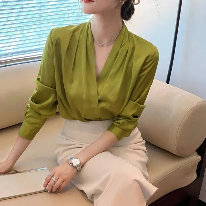 Woman wearing olive green blouse and beige skirt sitting on beige sofa with silver watch and rings