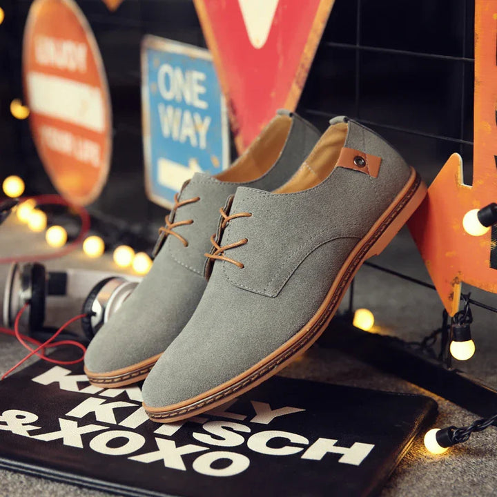 Gray suede casual shoes with brown laces and sole displayed with street signs and string lights