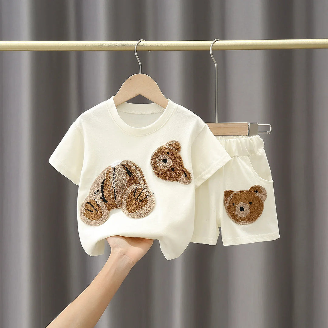 Cream kids outfit with teddy bear applique patch on shirt and shorts hanging on wooden hangers