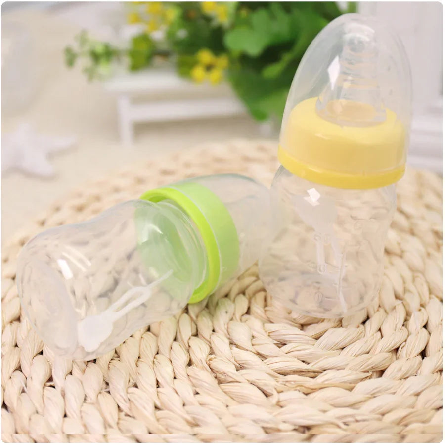 Two clear baby bottles with yellow and green caps on woven mat, blurred green plant background