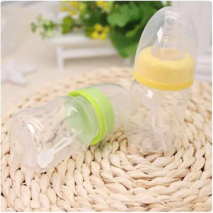 Two clear baby bottles with yellow and green caps on woven mat, blurred green plant background