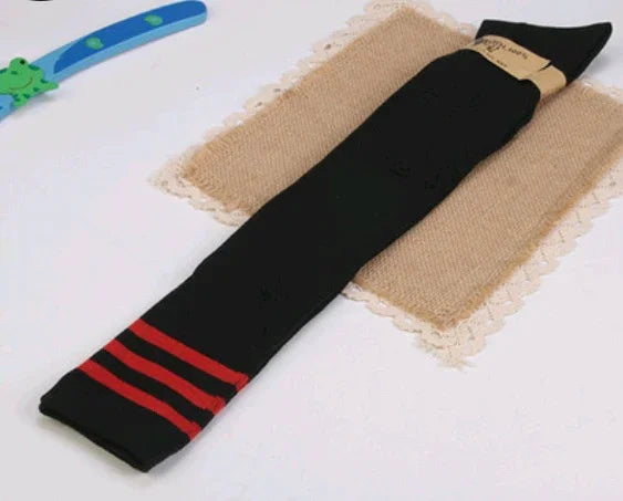Black knee-high socks with three red stripes at the top lying on a burlap cloth on a white surface