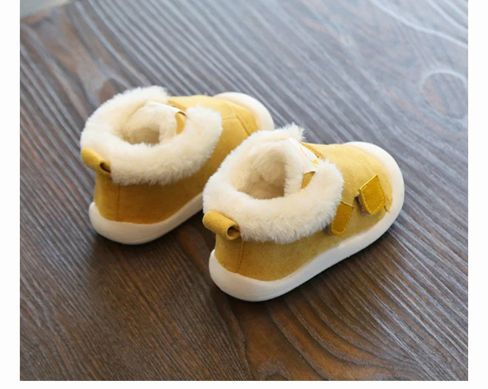 pair of yellow baby shoes with white fur lining and white soles on wooden floor
