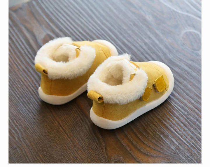 pair of yellow baby shoes with white fur lining and white soles on wooden floor