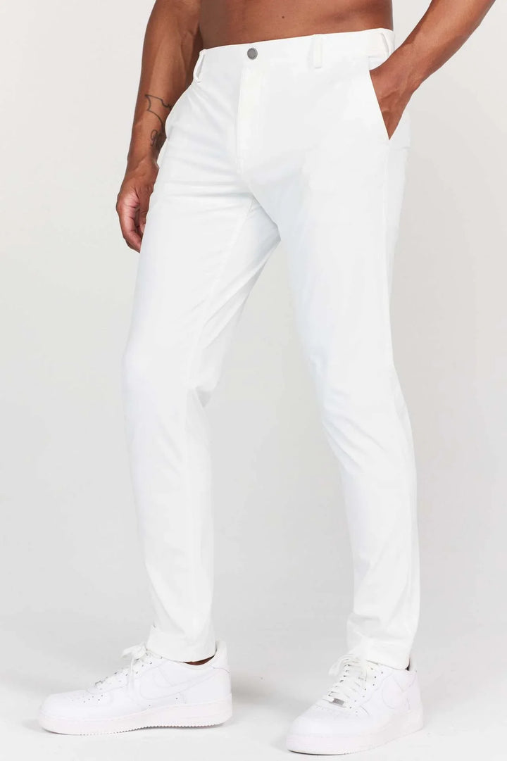 Man wearing slim fit white pants and white sneakers, with hand in pocket and visible arm tattoo