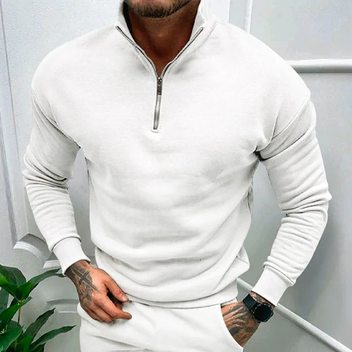 man wearing white quarter-zip sweatshirt with long sleeves and watch on wrist in minimalist indoor setting
