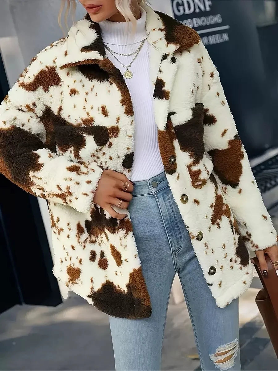 woman wearing a white, brown, and black spotted fleece coat over a white turtleneck sweater and light blue ripped jeans